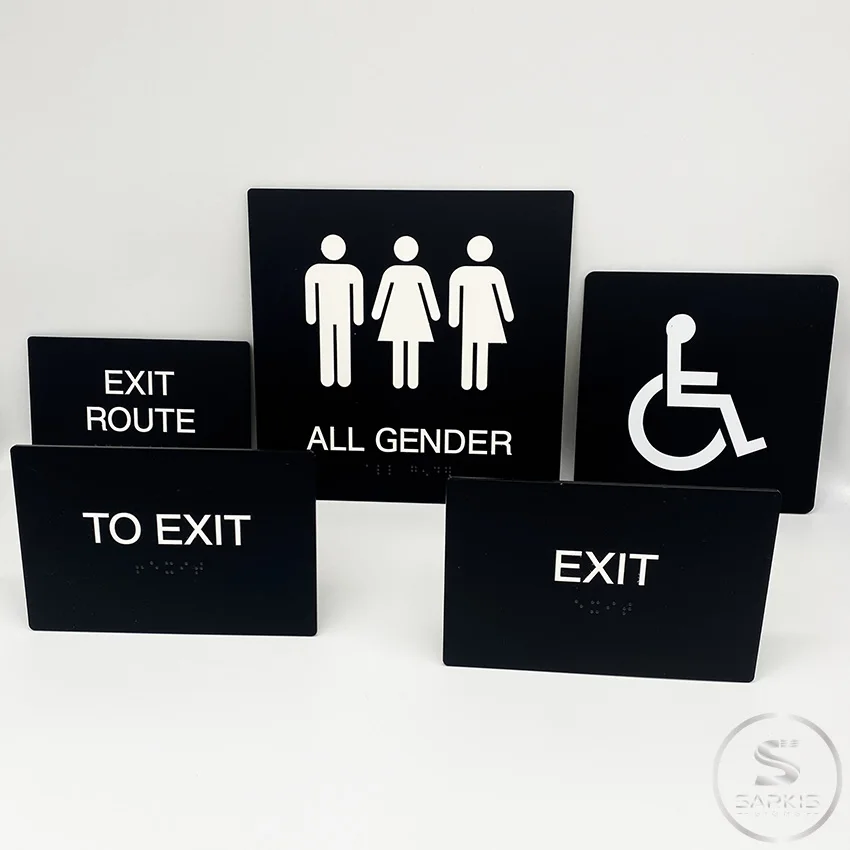 Black accessible restroom, exit and directional signs with white lettering and symbols