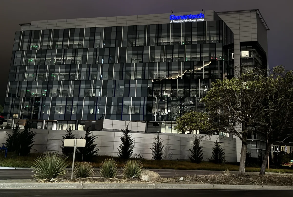 Illuminated Genentech sign on a glass office building at night